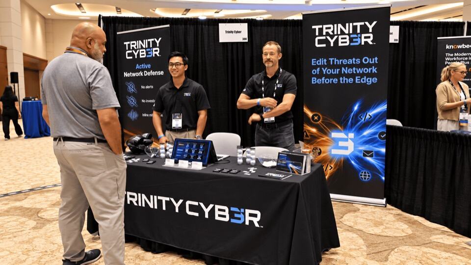 Team members talking with a visitor at the Trinity Cyber booth
