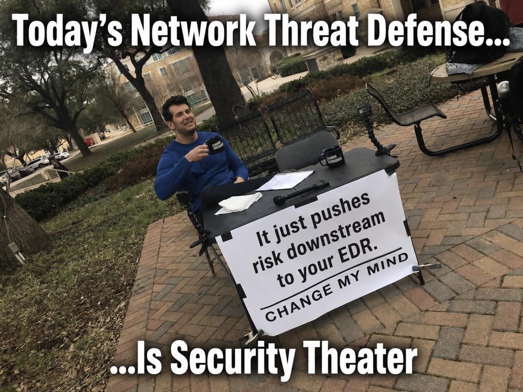 “Change My Mind” Meme: a man seated at a table with a sign reading ‘Today’s network-based protection is security theater — it just pushes risk downstream to your EDR. Change my mind.’